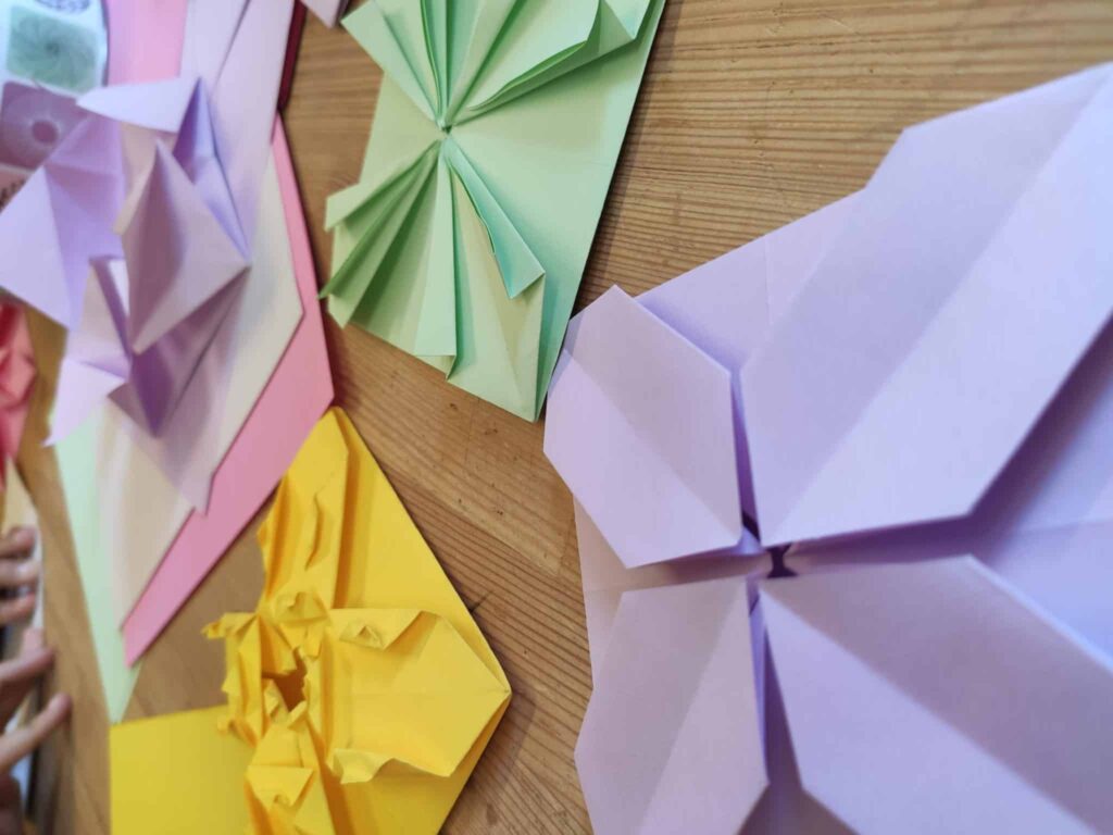 Papeles de colores plegados sobre una mesa, una propuesta de papiroflexia para explorar geometría, simetría, secuencias y matemáticas sin fichas.